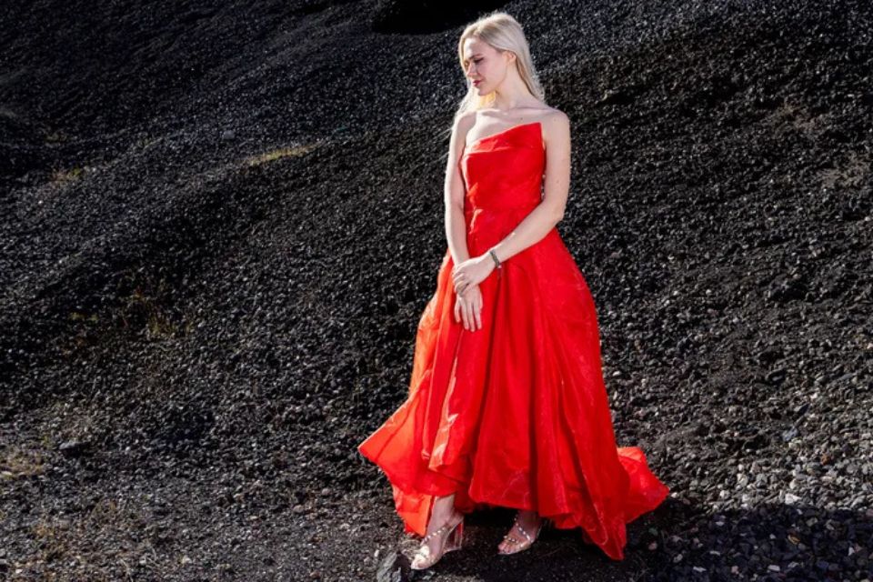 A young woman wearing a red dress stands in a rocky landscape