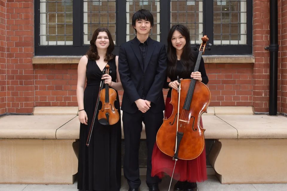 A young man and two young women wear black, the women hold a violin and cello