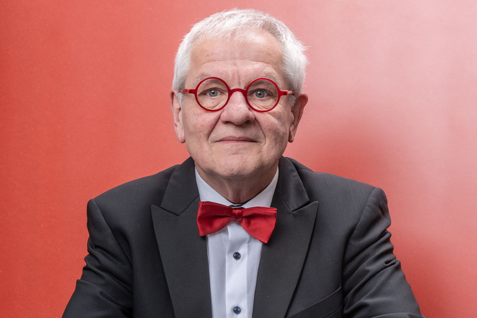Reinhard Goebel wears a black suit with a red bow-tie and red glasses