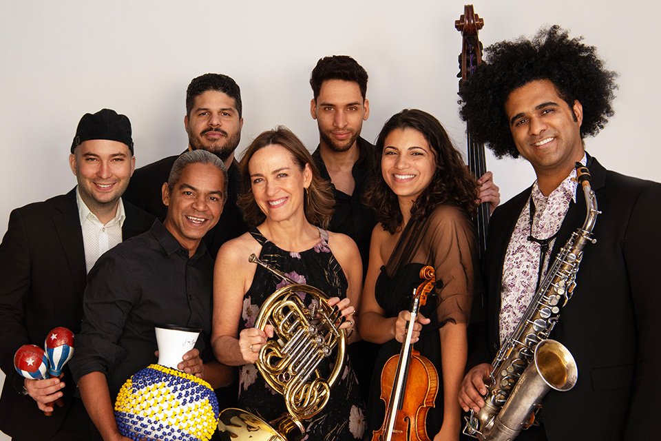 A group of people stand in a huddle smiling and holding a range of musical instruments