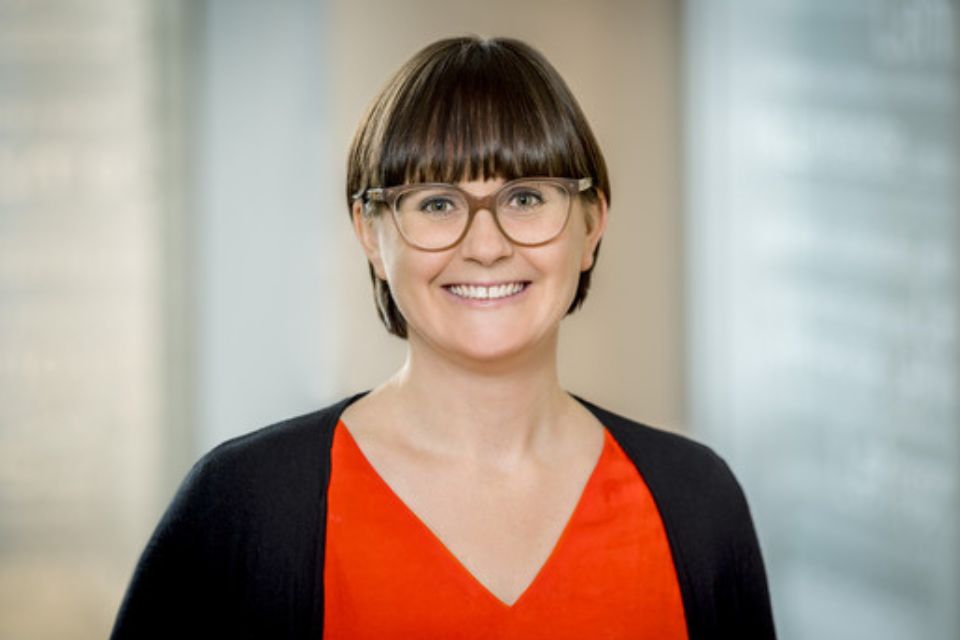 Sarah Slater wears an orange top and glasses and smiles