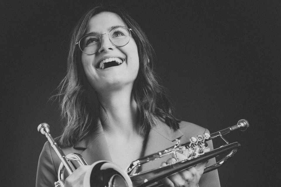 Selina Ott holds her trumpet and looks up, laughing