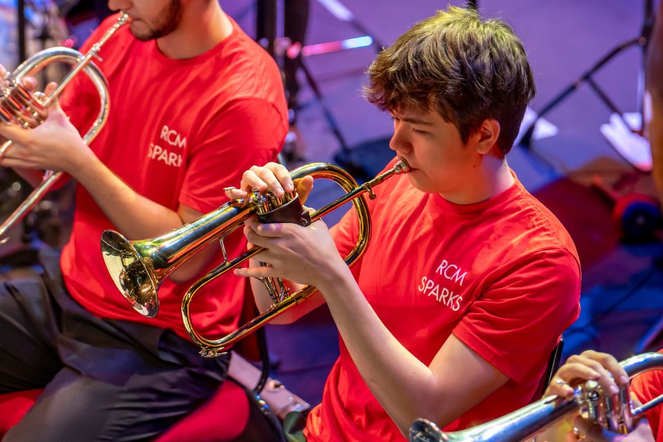 A young man wears a red t-shirt and plays the trumpet on stage