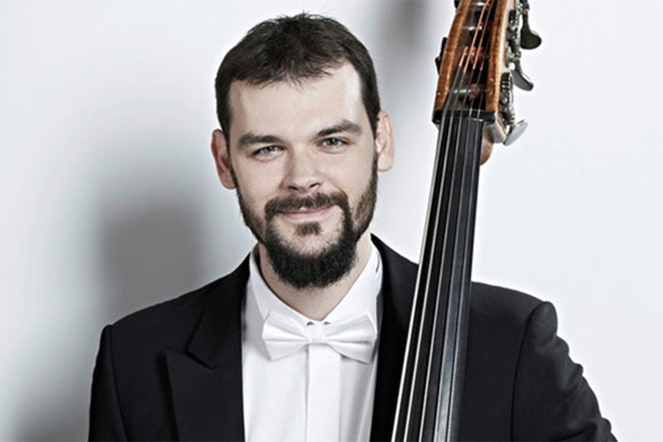 Stanislau Anishchanka, wearing a black jacket and white bow tie, smiles with his double bass