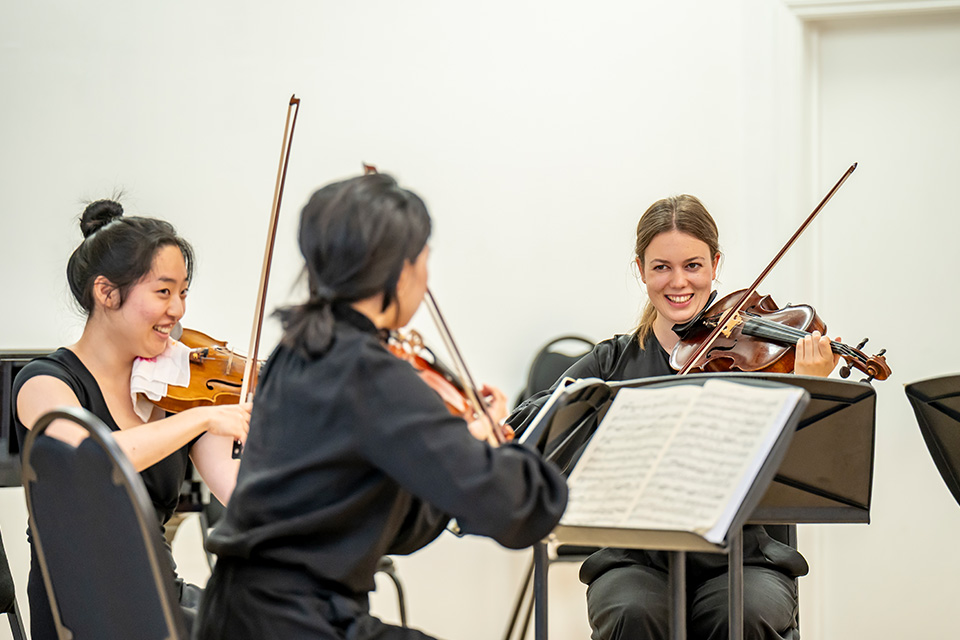 A string quartet laugh as they hold their instruments on stage