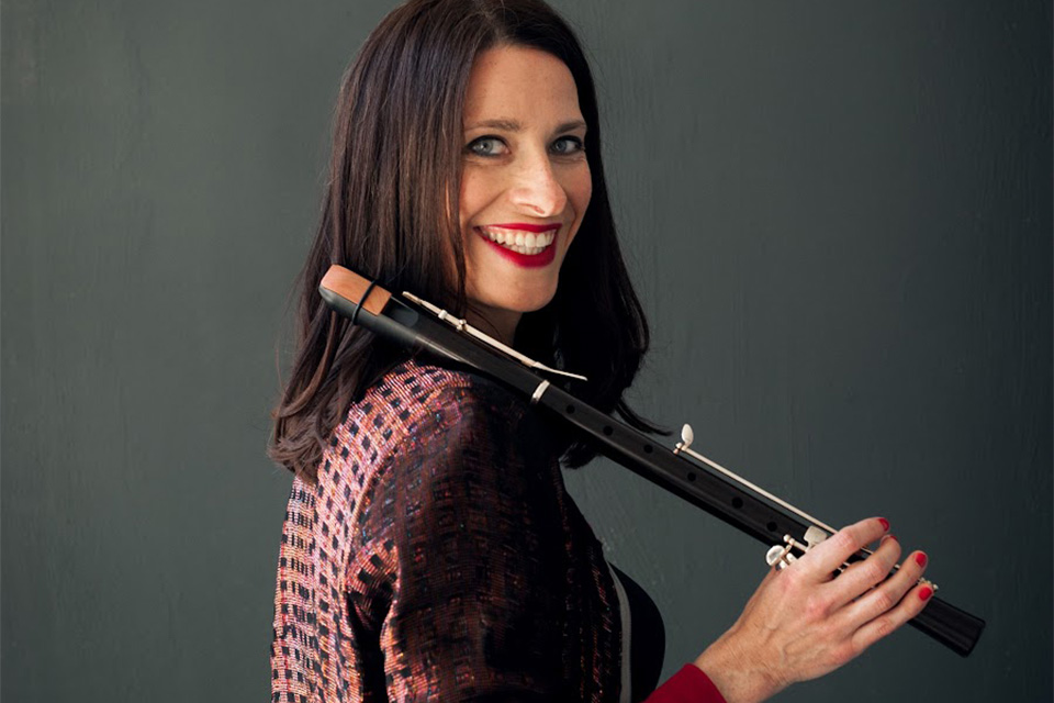 Susanne Fröhlich stands side on to camera, holding a recorder to her shoulder and smiling