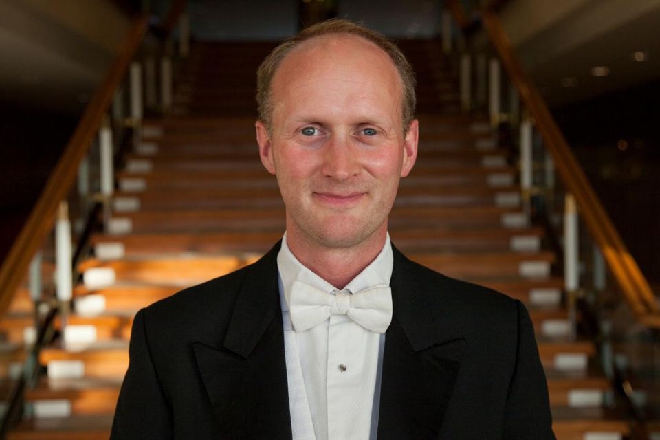 Timothy Rundle wears a suit dinner jacket in front of a large staircase