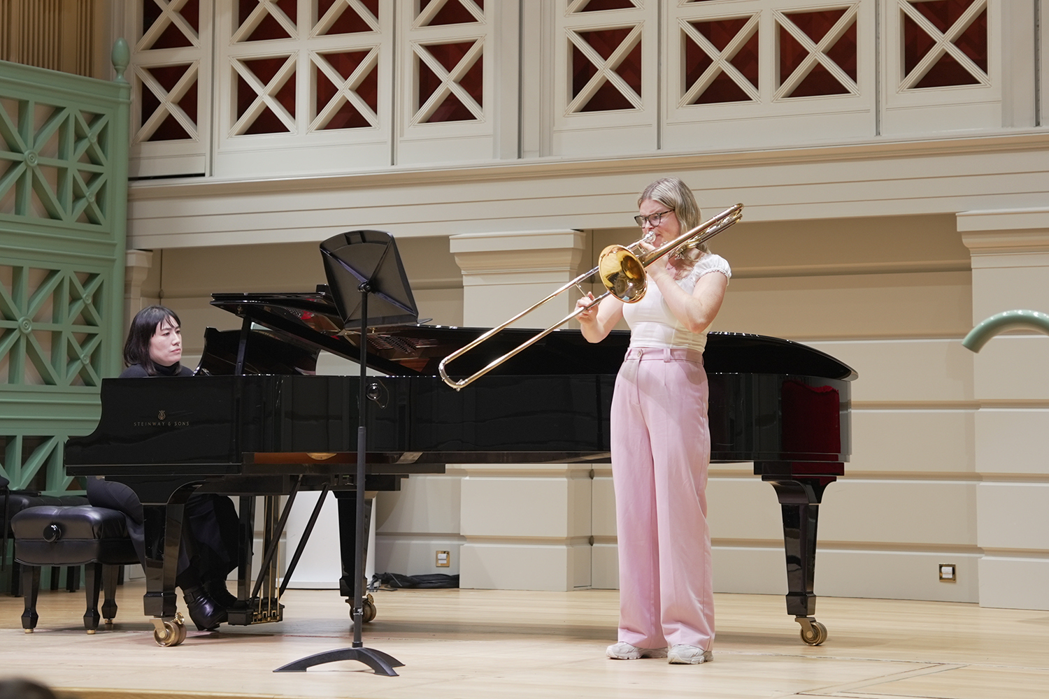 A trombonist wearing light pink trousers performing in the Performance Hall with a pianist accompaniment
