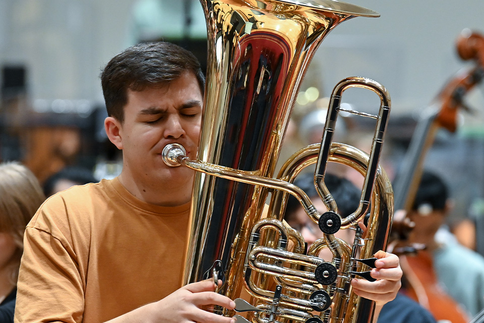 A young man wearing an orange tshirt plays the tuba