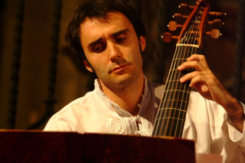 A man with dark hair wearing a white shirt performing on a viol