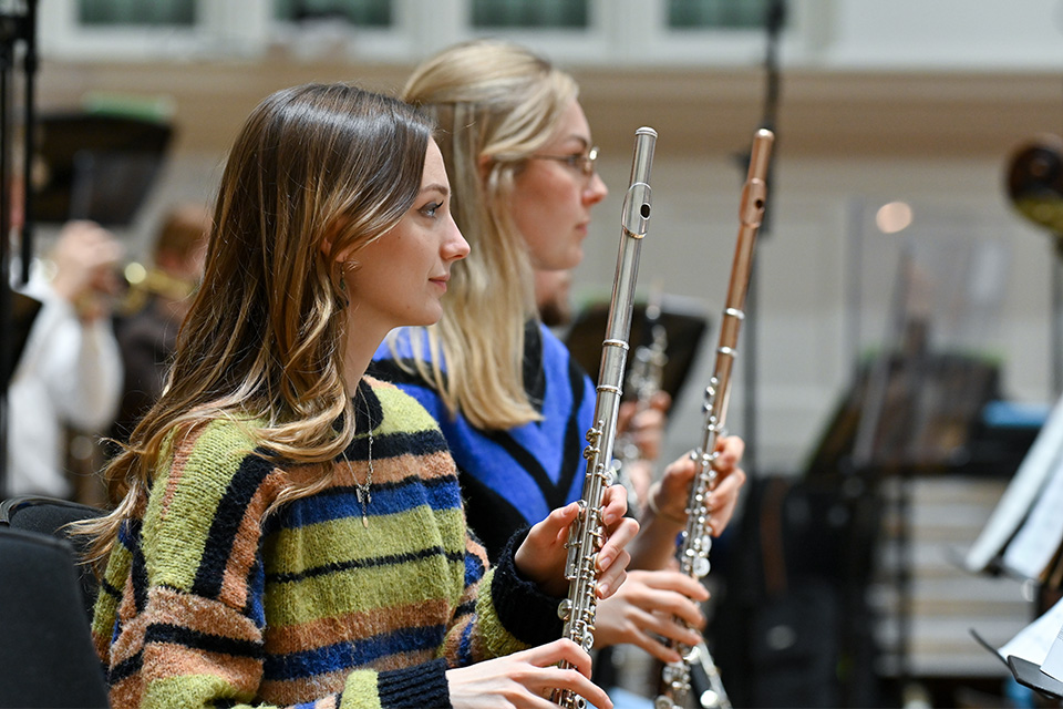 Two young women hold flutes in an orchestra on stage