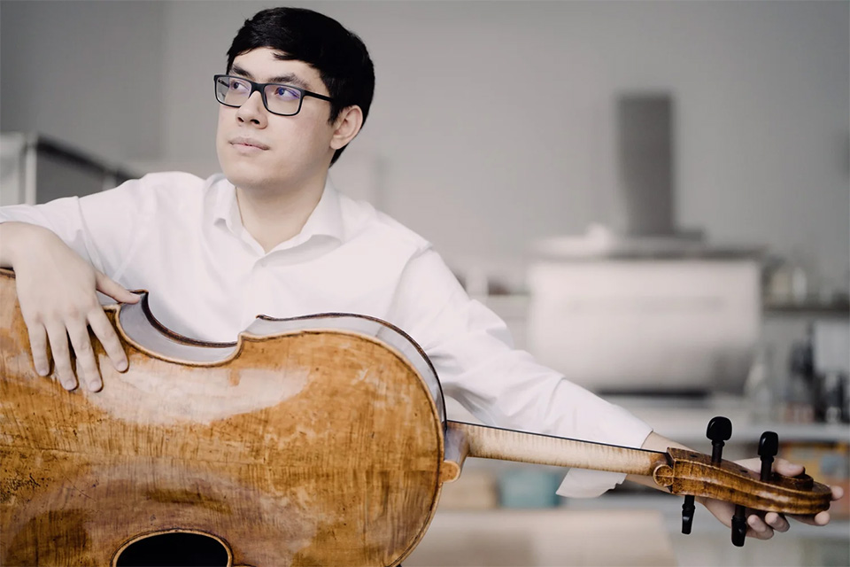 Zlatomir Fung holds his cello whilst wearing a white shirt and looking upwards