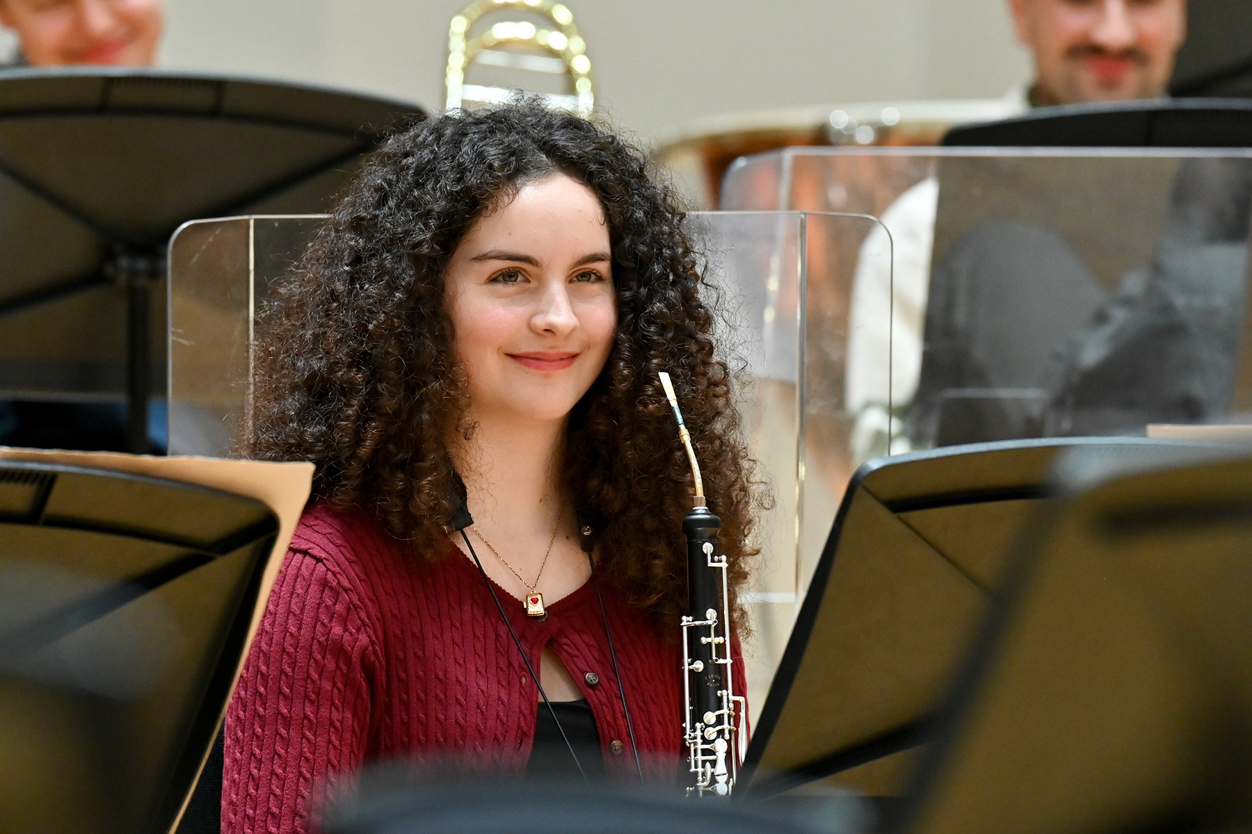 A female student holding her oboe, sitting in an orchestra rehearsal.