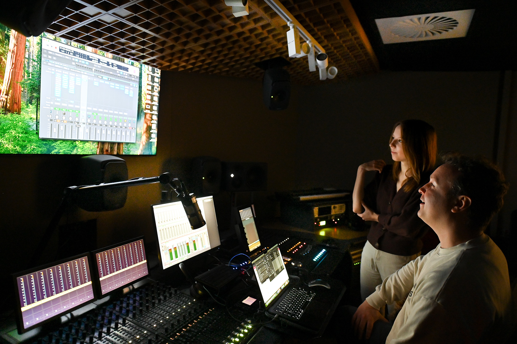 Two students smiling and looking at a screen in a studio.