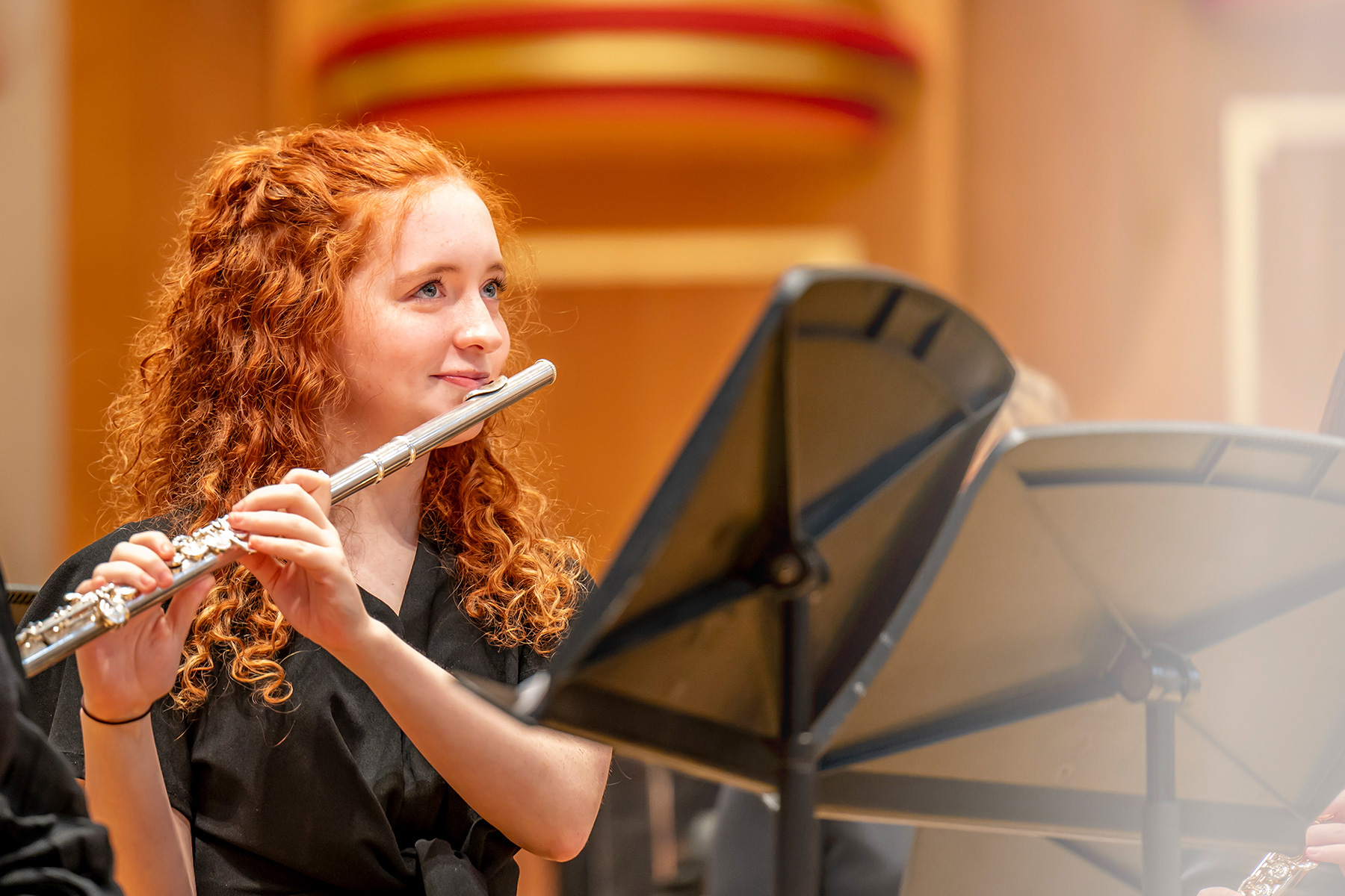 A female student with red hair, playing the flute in a rehearsal performance.
