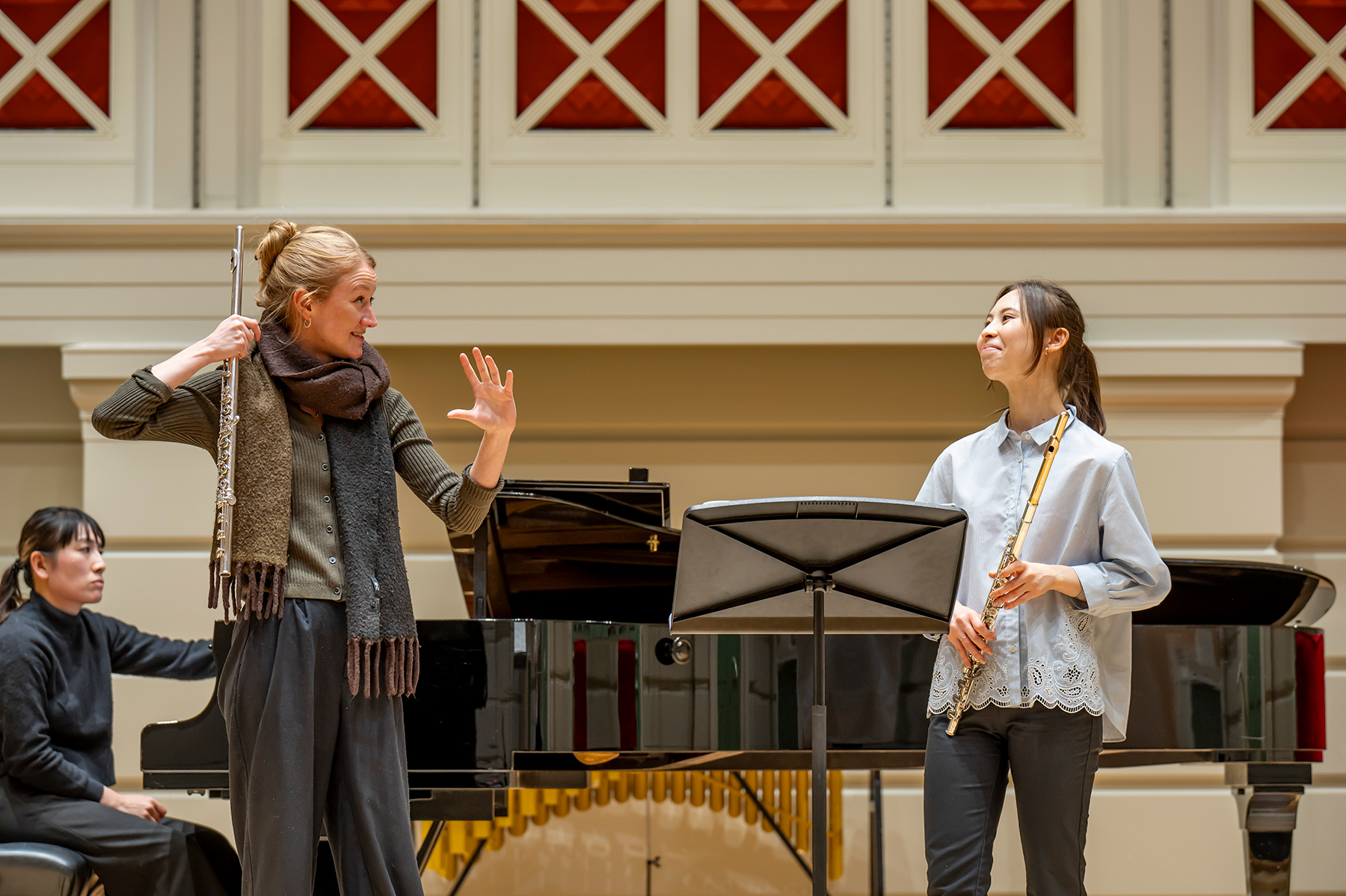 A female professor leading a flute student during a performance on stage.