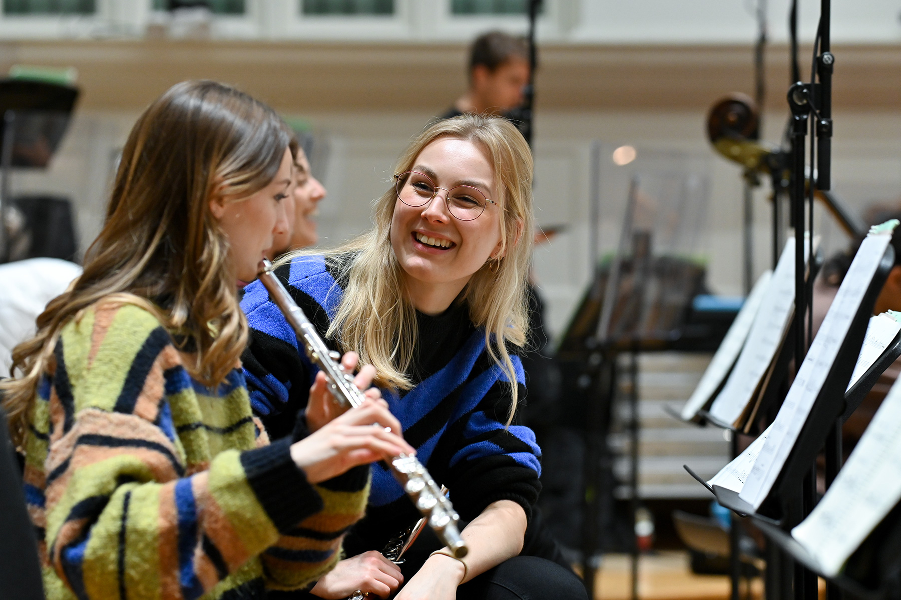 Two female students in an orchestra rehearsal together.