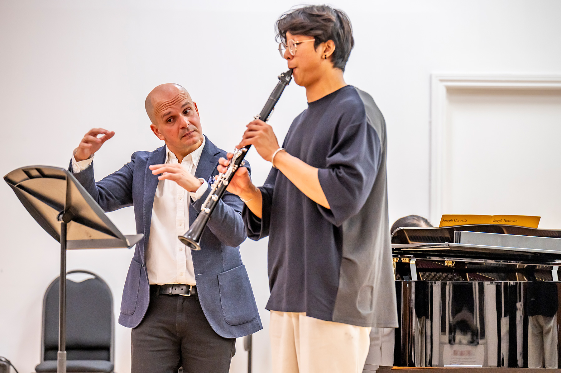 A male student playing the clarinet, with a male teacher guiding the student in a performance.