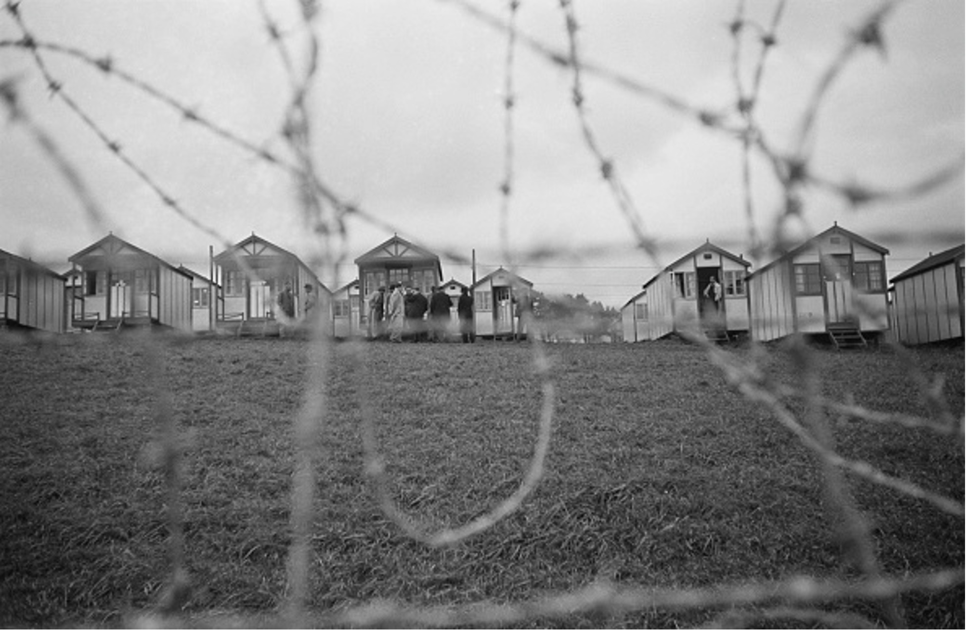 Black and white photograph of an internment camp in England seen through barbed wire, c. 1940