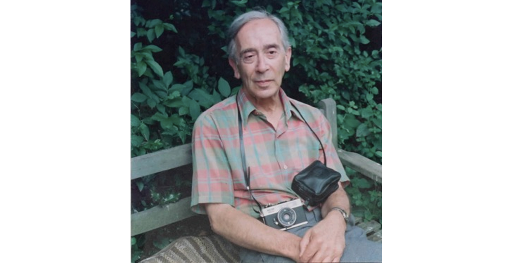 Val Kennedy, a grey-haired man, wearing a colourful short sleeved shirt, with a camera around his neck.