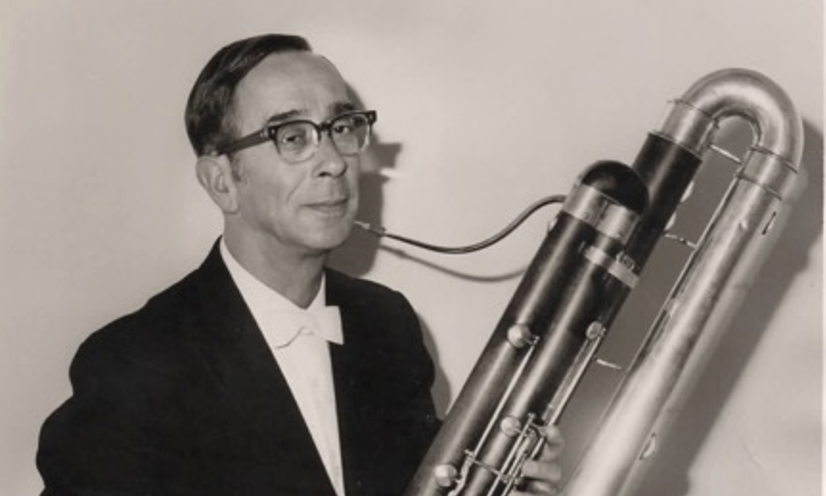 Black and white photo of Val Kennedy, a white man, holding a musical instrument; wearing formal black attire and wearing spectacles.