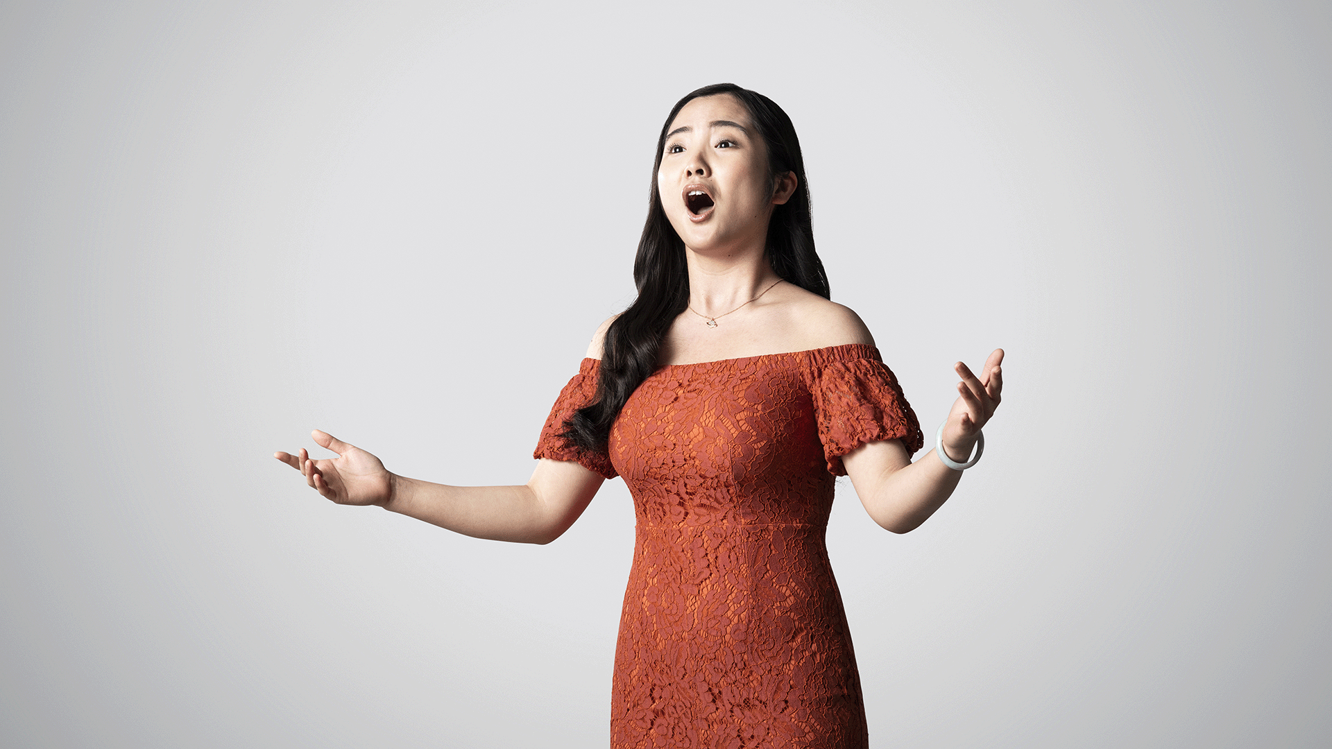 An RCM student in a red dress singing, against a grey background